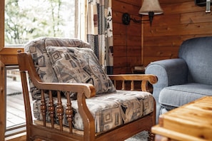 Una silla de madera con cojines estampados y un sofá azul en una habitación con paredes de madera y un ventanal.