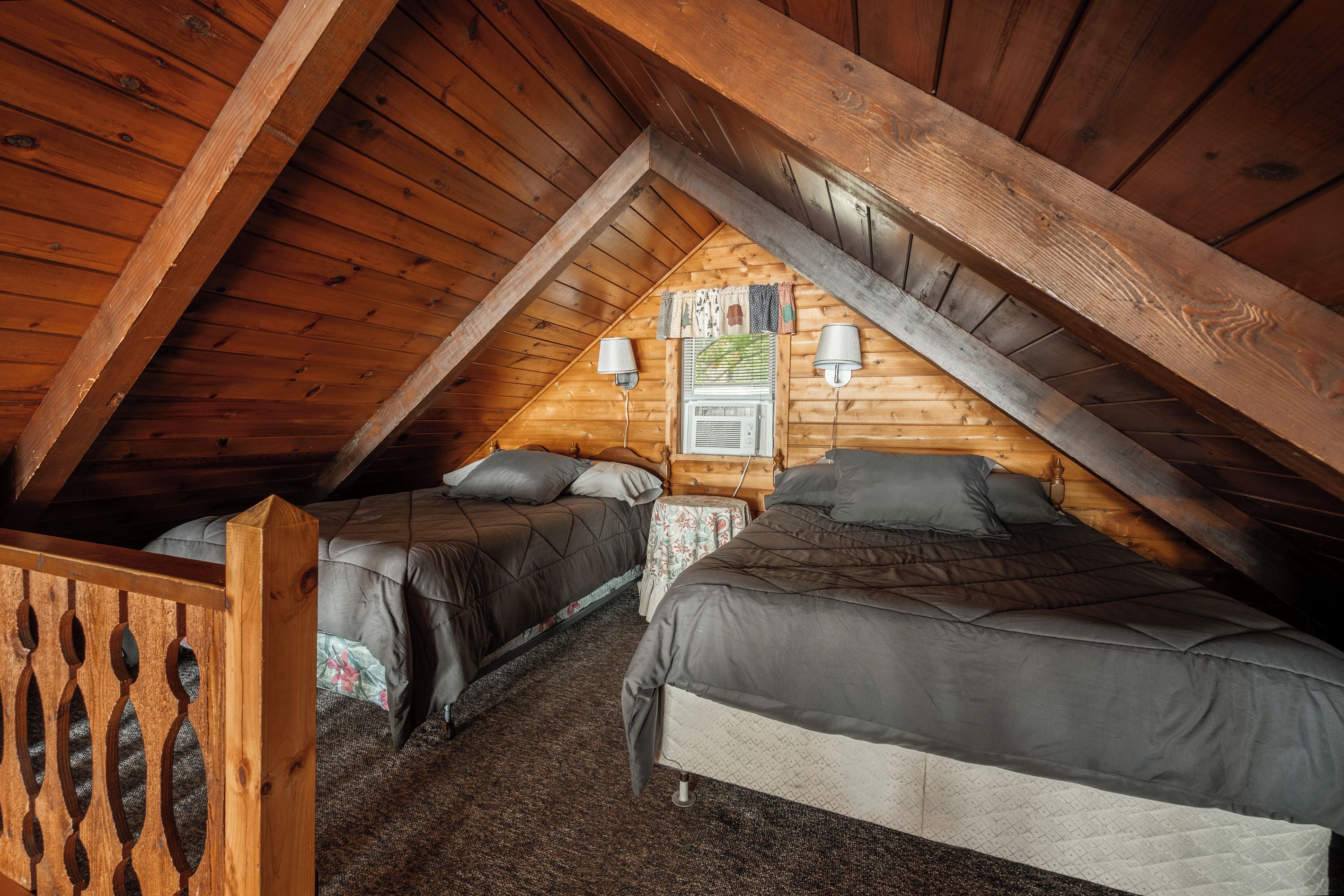 Une chambre mansardée chaleureuse avec deux lits, un plafond en bois et une petite table avec une lampe.