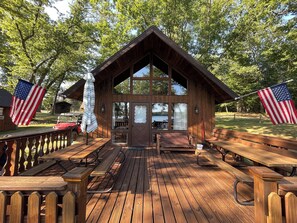 A wooden cabin with a deck, picnic tables, and American flags.