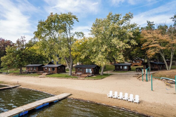 A lakeside cabin area with wooden structures, a dock, and beach chairs.