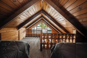 A cozy attic bedroom with a sloped ceiling, a wooden balcony railing, and two beds.