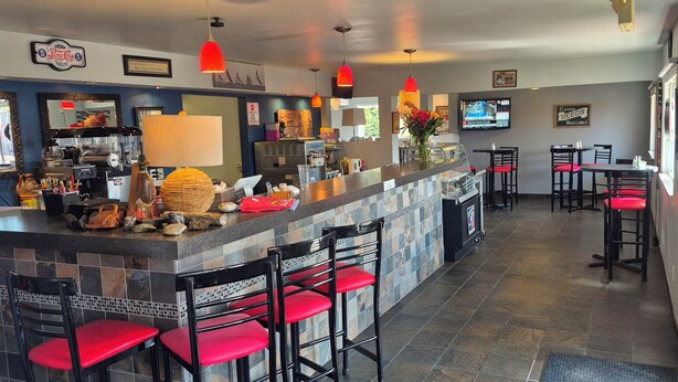 A bar area with a counter, red bar stools, and a television screen. - LaniKai Hotel & Restaurant (Batchewana Bay)