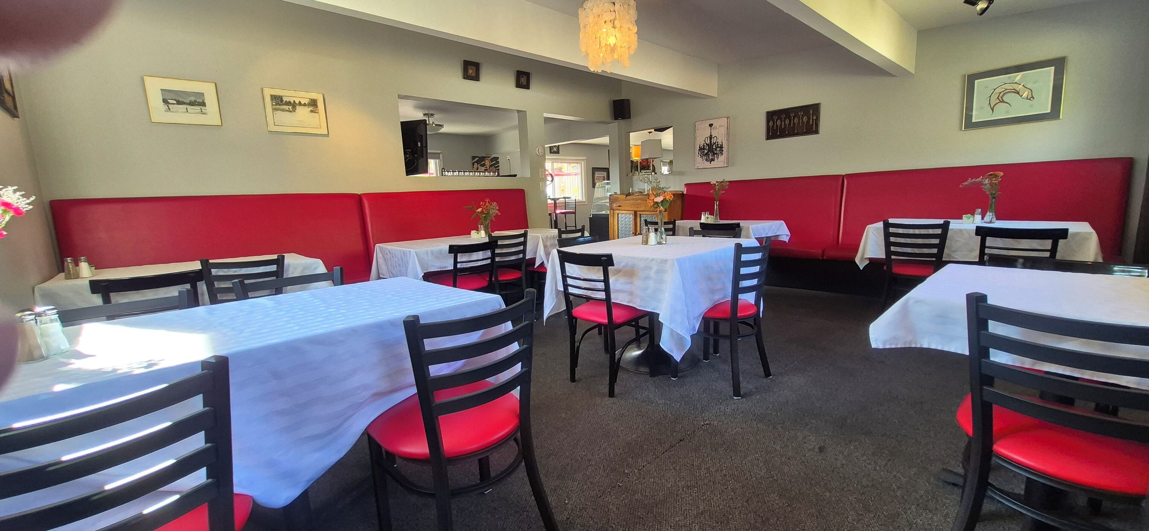A restaurant interior with booths and tables, red and white decor, and framed pictures on the walls.