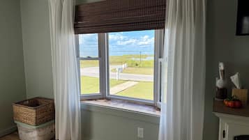 A room with a large window, a wicker basket, a white trash bin, and a small table with a tissue box and decorative items.