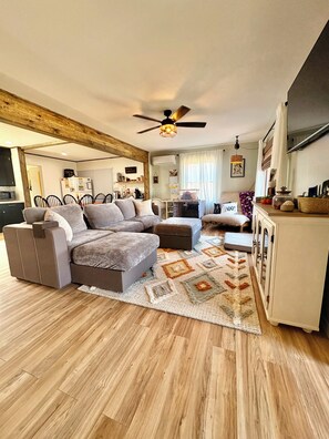 A modern living room with a sectional sofa, a dining area, and a ceiling fan.