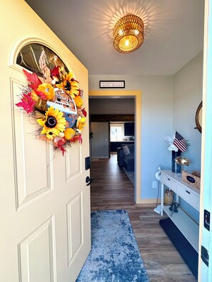 A hallway with a decorative wreath, a sign reading 'There's no place like home,' and a chandelier. - Charming 2 Bedroom house in beautiful Smith Island Pet-Friendly (Smith Island)
