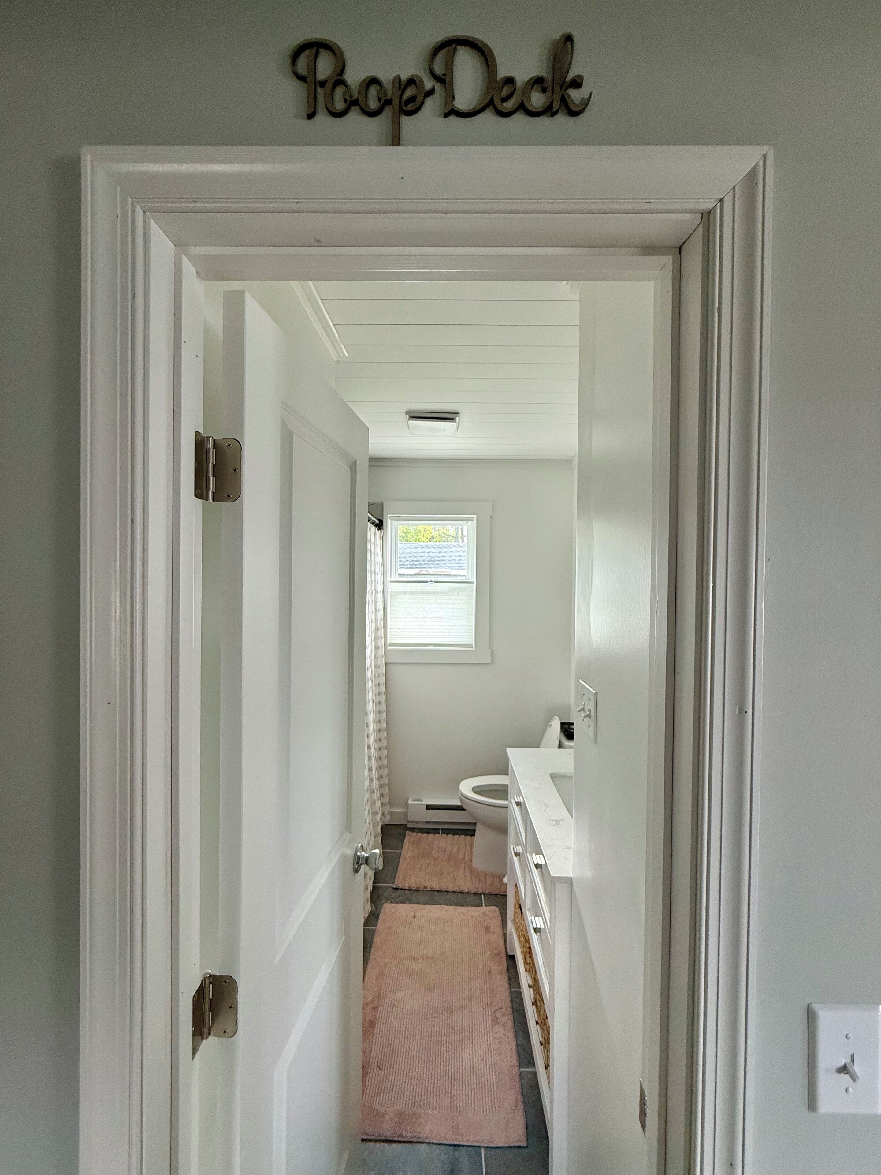 A hallway leading to a bathroom with a toilet, sink, and a window.