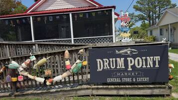 A sign for Drum Point Market with a general store and eatery, a wooden fence, and a red-roofed building in the background.