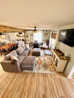 A living room with a sectional sofa, ottoman, dining table, chairs, and a television.