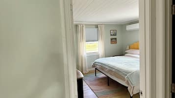A bedroom with a bed, a window with curtains, a painting on the wall, and a sign above the door reading "Captains Quarters".