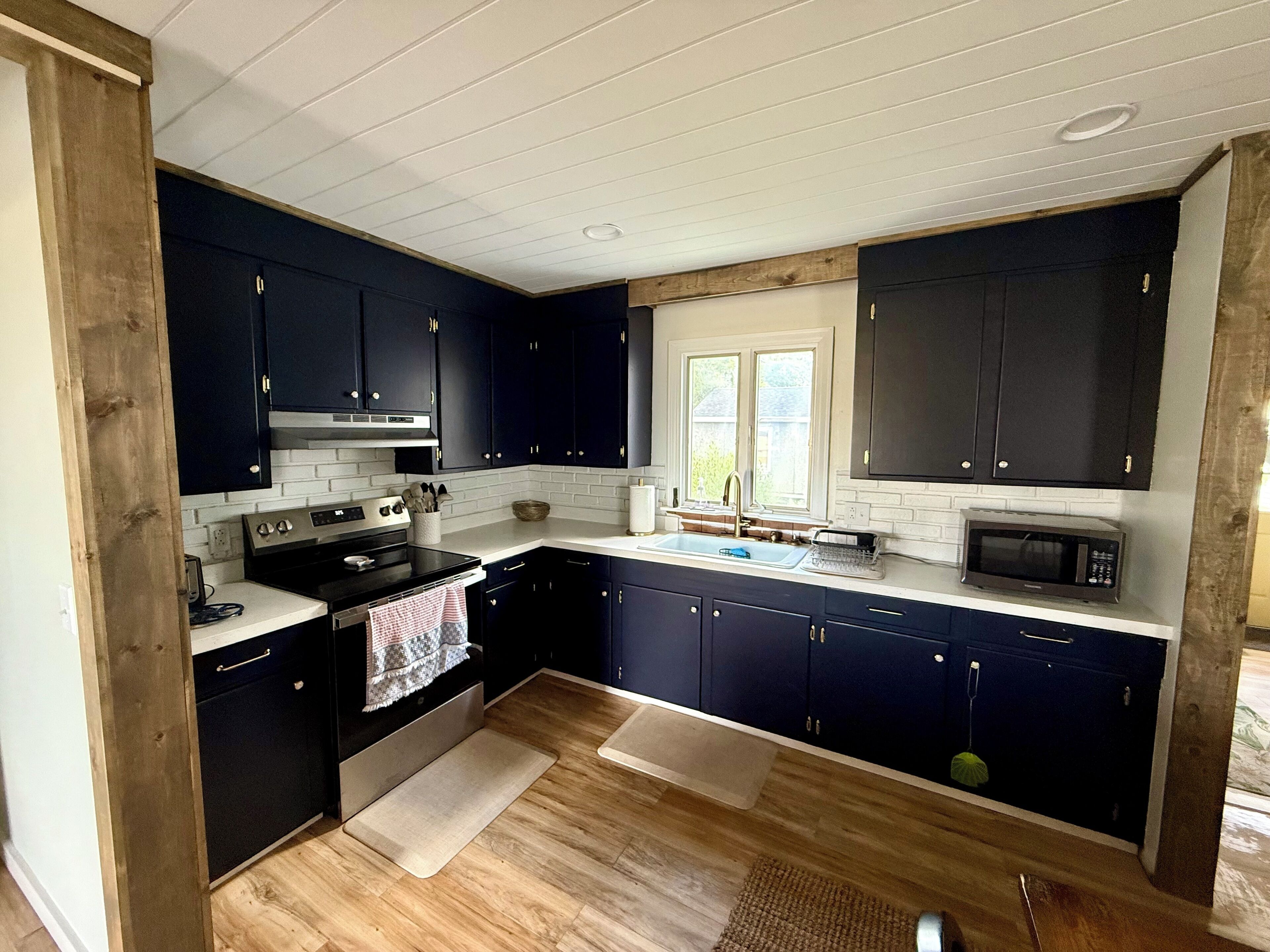 A modern kitchen with dark blue cabinets, white countertops, a stainless steel stove, and a microwave.