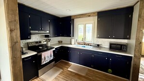 A modern kitchen with dark blue cabinets, white countertops, a stainless steel stove, and a microwave.