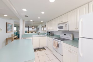 A modern kitchen with white cabinets, a central island, and a view to the living area.