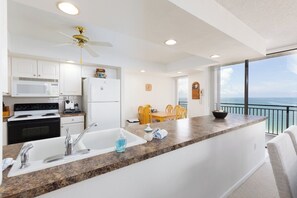 A modern kitchen with white cabinets, a granite countertop, and a view of the ocean through large windows.