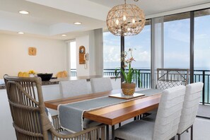 A dining area with a wooden table, grey upholstered chairs, and a woven pendant light. - Spectacular Gulf Views (Treasure Island)