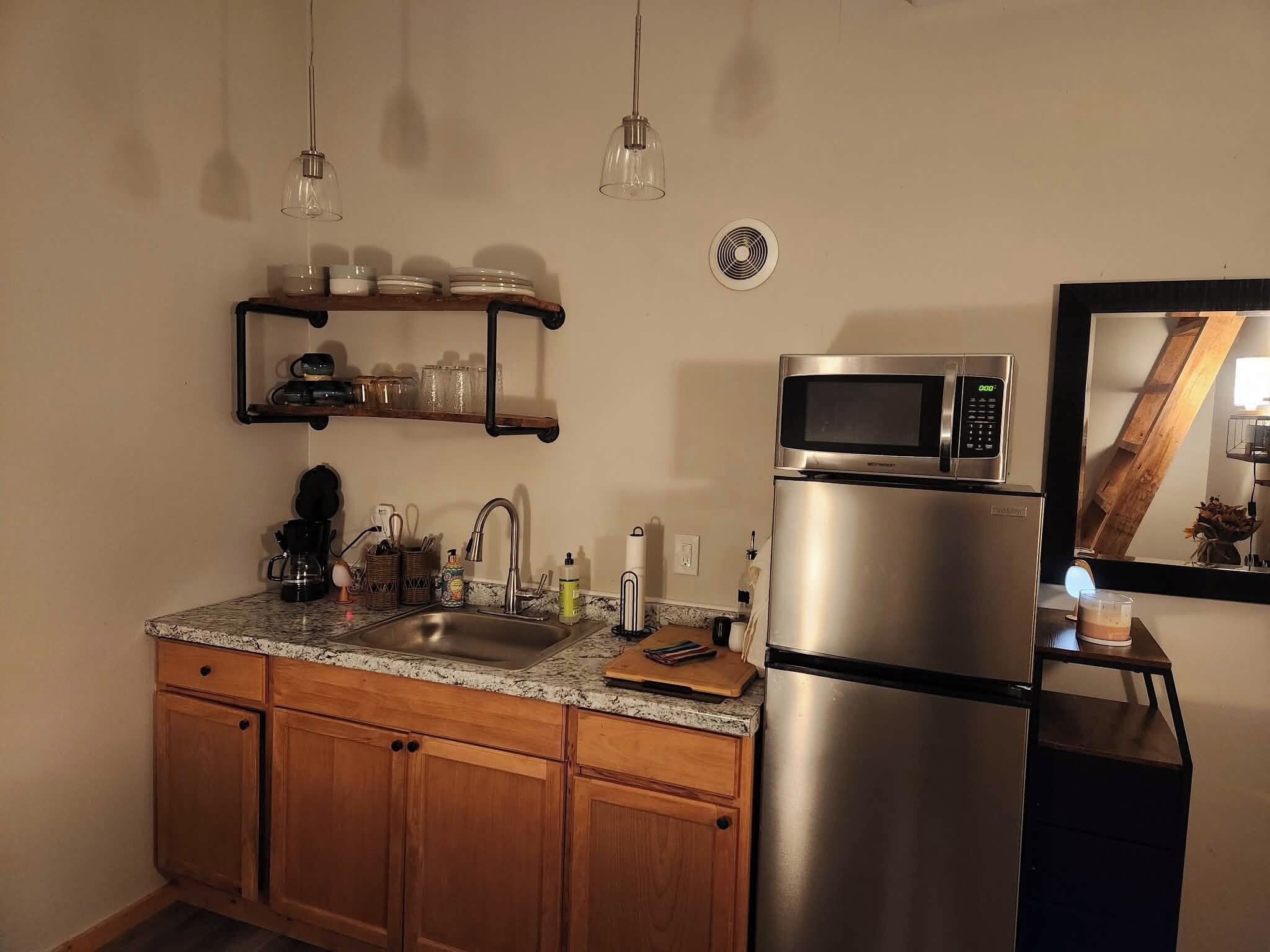 Een keuken met houten kastjes, een roestvrijstalen koelkast, een magnetron, een spoelbak en hangende hanglampen.
