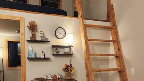 A loft-style bedroom with a wooden ladder, a bed, a dresser, and a wall clock.