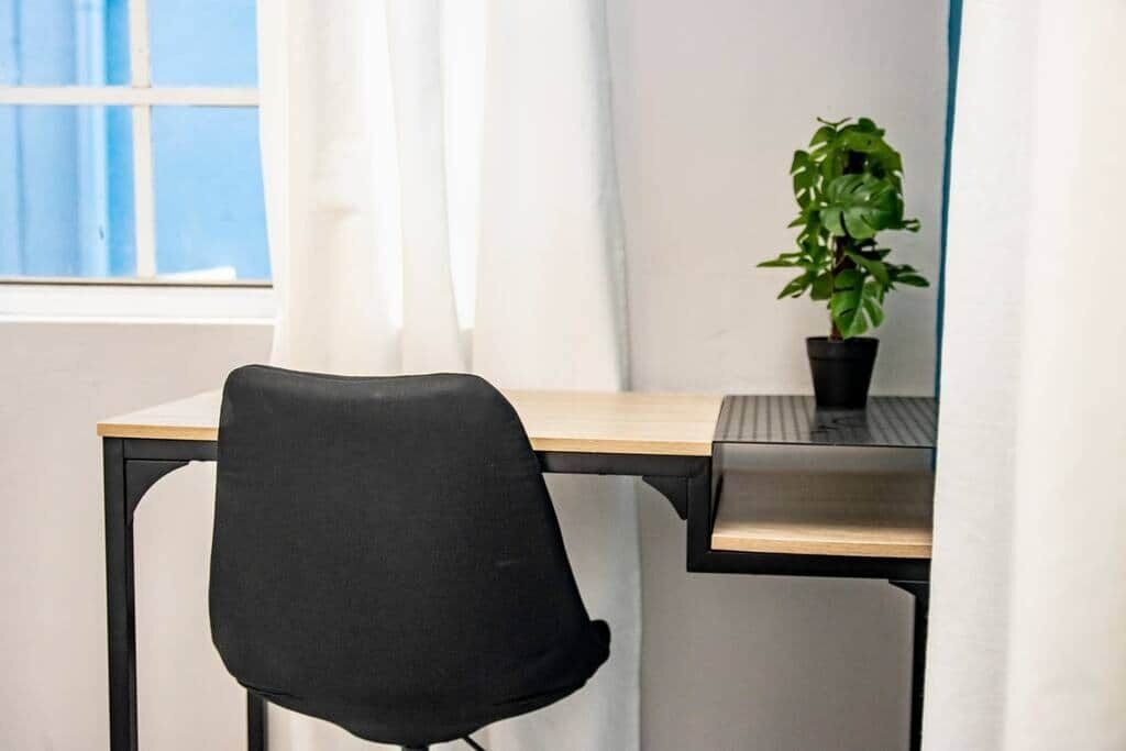 Ein Arbeitsplatz mit einem schwarzen Bürostuhl, einem Holztisch und einem Blumentopf.