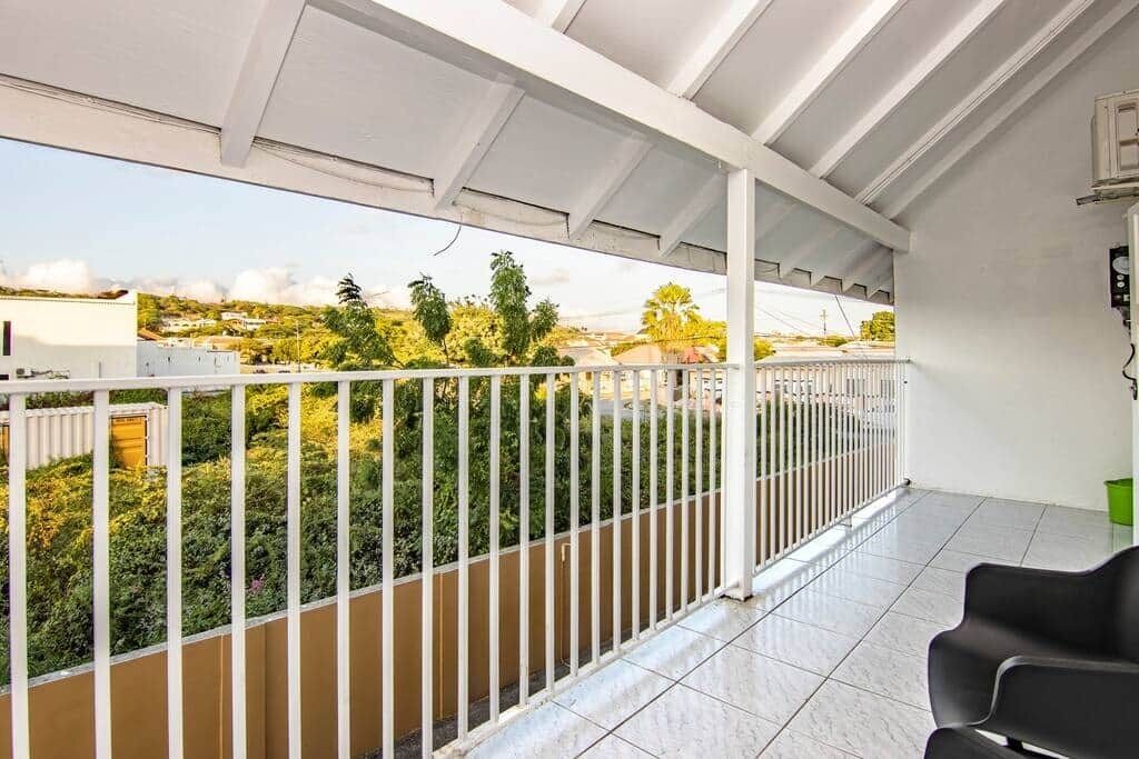 Un balcone con ringhiera bianca, pavimento piastrellato e vista su un paesaggio verde.