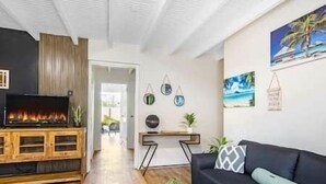 A modern living room with a fireplace, a black sofa, and a wooden coffee table. - Citylife Apartments - Pool / Free Parking / in Willemstad. Apartment I (Willemstad)