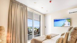 A hotel room with a bed, a television, a view of the ocean, and a balcony with outdoor seating. - LUX 3 BR Sub Penthouse One Mambo Beach (Willemstad)
