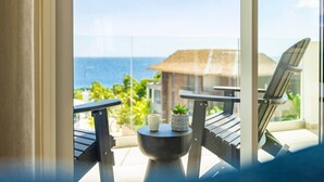 A balcony with a view of the ocean, a chair, a small table with a plant and a cup, and a thatched-roof building in the background. - LUX 3 BR Sub Penthouse One Mambo Beach (Willemstad)