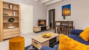 En moderne stue med sofa, sofabord, fjernsyn og et spiseområde med stole.