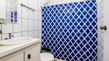 A bathroom with a white sink, a mirror, a toilet, and a shower with a blue patterned curtain.