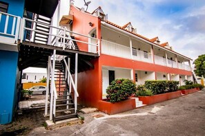 Un edificio de dos pisos con fachada roja, balcones blancos y una escalera que conduce al nivel superior.