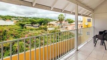 A balcony with a metal railing, a yellow wall, and a view of a residential area with houses and greenery.