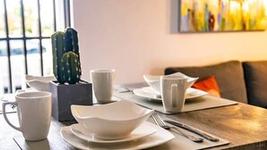 Una tavola imbandita con piatti, tazze e posate bianche, con un cactus in vaso sulla sinistra.