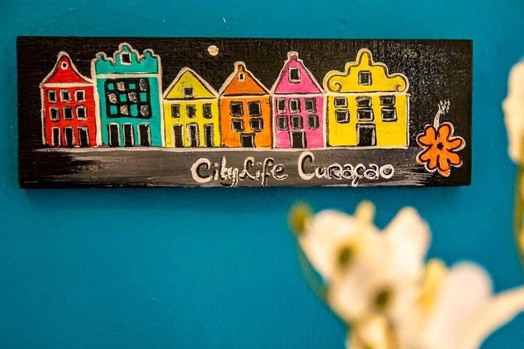 Ein farbenfrohes Schild mit dem Schriftzug 'City Life Curacao' und einer Blume.