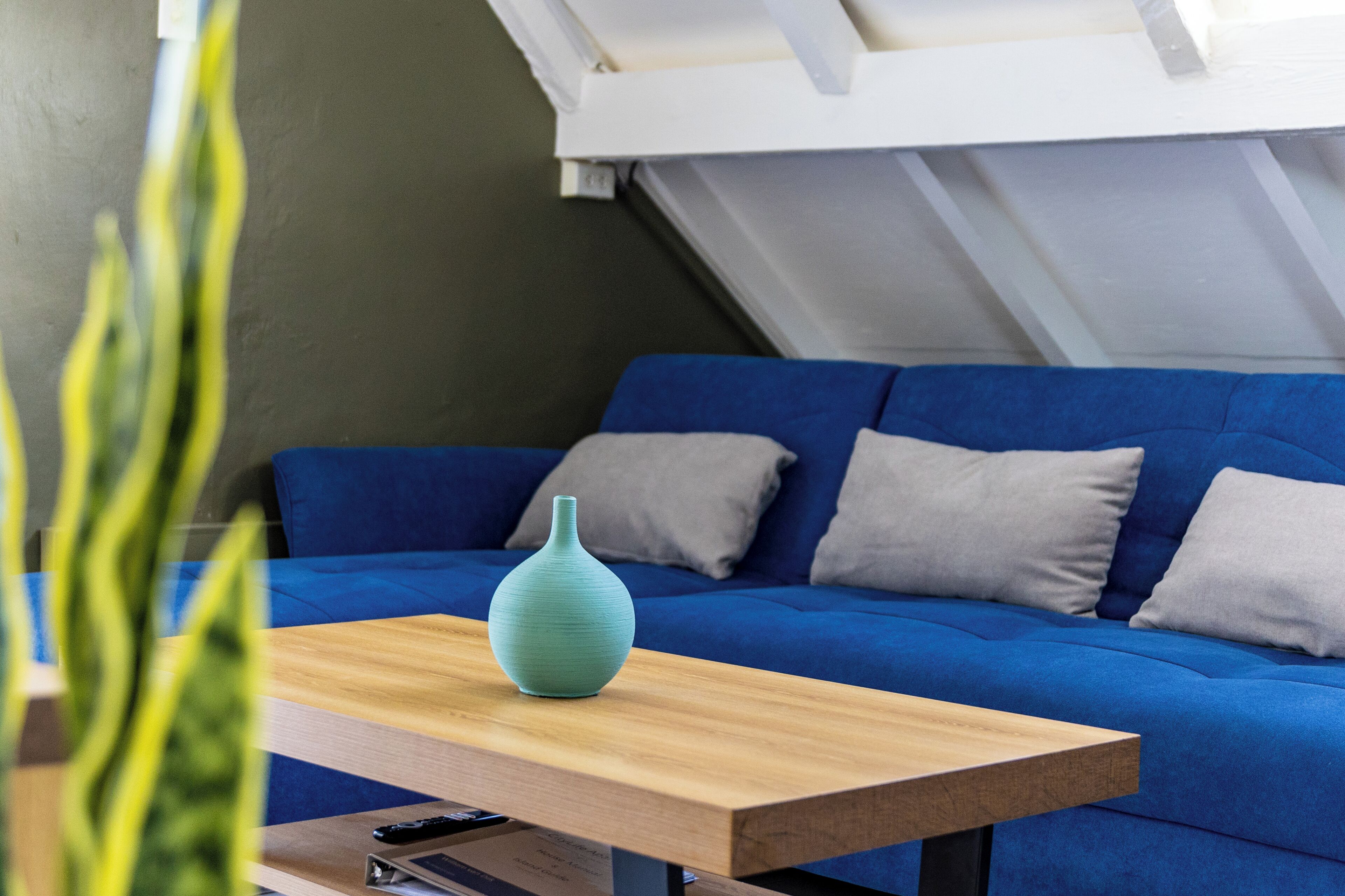 A modern living room with a blue sofa, a wooden coffee table, and a green vase.