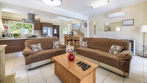A spacious living area with two brown sofas, a wooden coffee table, and a kitchen in the background. - Villa Alexander - Three Bedroom Villa, Sleeps 6 (Paralimni)