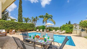 An outdoor pool area with a table set for dining, surrounded by lounge chairs and a large umbrella. - Villa Alexander - Three Bedroom Villa, Sleeps 6 (Paralimni)
