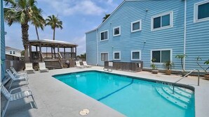 Une piscine avec des chaises longues, un espace de détente couvert et un bâtiment doté de nombreuses fenêtres.