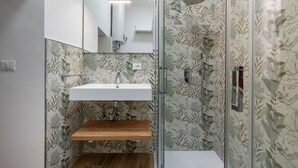 Une salle de bain avec une douche à parois de verre, une étagère en bois, un lavabo blanc et un miroir.