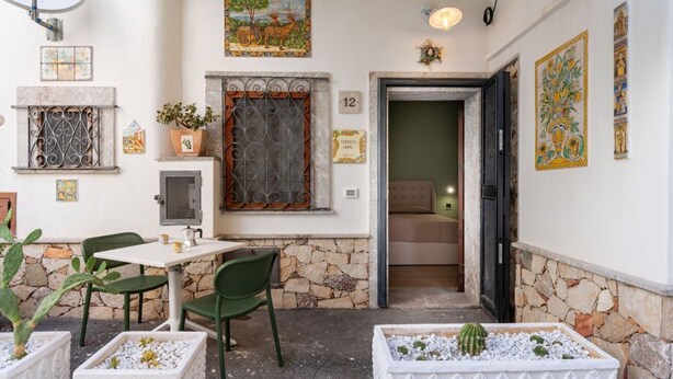 Une petite pièce avec un mur en pierre, une fenêtre ornée de barreaux en métal, une porte et une petite table avec des chaises.