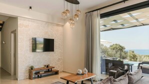 Una sala de estar moderna con un televisor de pantalla plana montado en una pared con textura, una mesa de centro de madera, un sofá y una lámpara colgante.