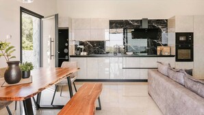 Una cocina moderna con encimera de mármol, horno empotrado y comedor con mesa y banco de madera.