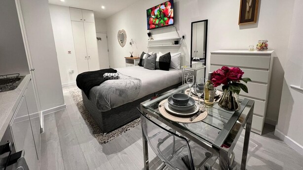 Un dormitorio moderno con cama, mesita de noche, cómoda y televisor montado en la pared.