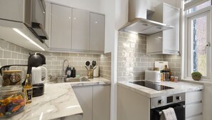 Una cocina moderna con armarios blancos, encimera de mármol y horno empotrado.