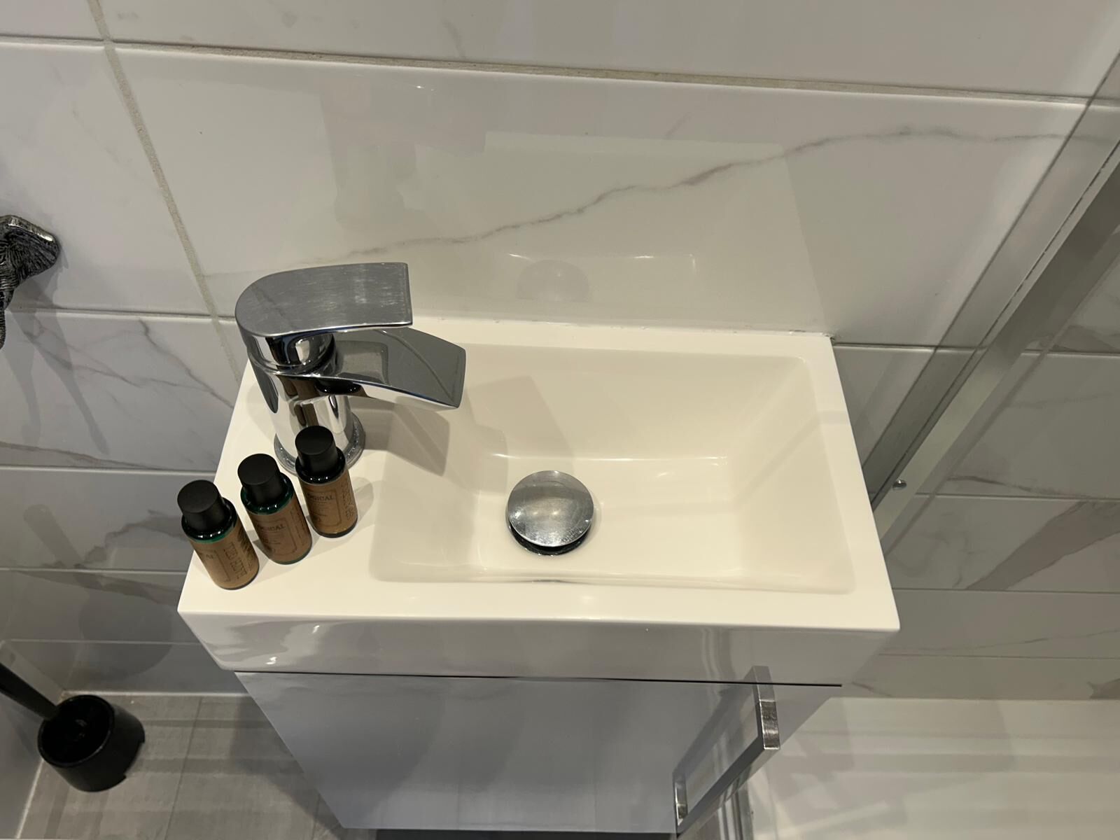 A bathroom with a white sink, a modern faucet, and three bottles of soap.