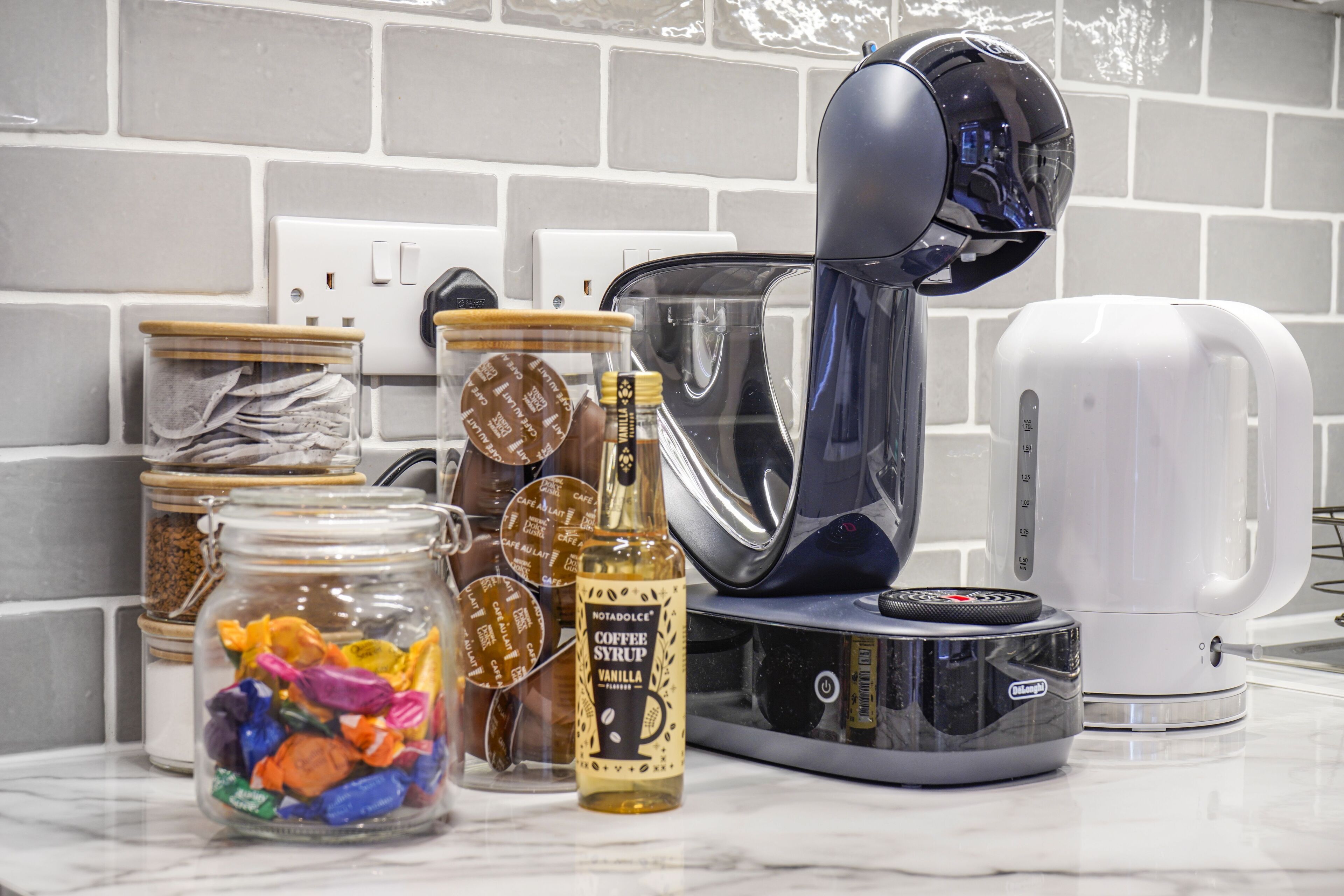 Un comptoir de cuisine avec une machine à café, des bocaux de collations et une bouteille de sirop de café.