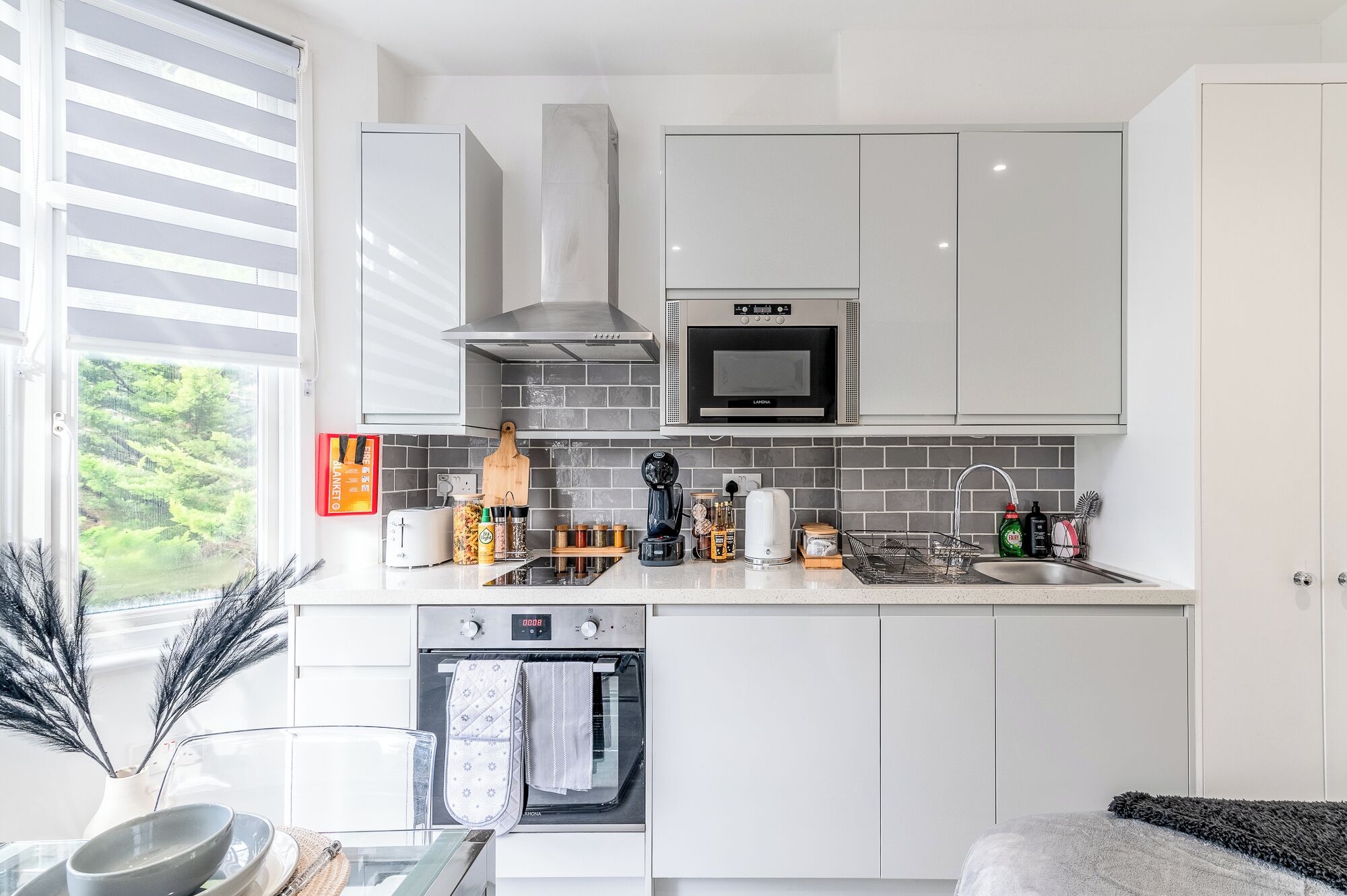 A modern kitchen with white cabinetry, a built-in oven, a microwave, and a stainless steel sink.