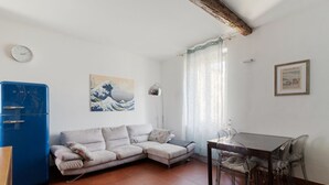 Una sala de estar con un sofá, una mesa de comedor con sillas, un refrigerador azul, un reloj de pared y un cuadro.