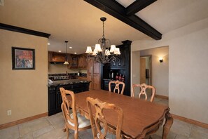 Un espace repas avec une table et des chaises en bois, un lustre et une cuisine en arrière-plan.