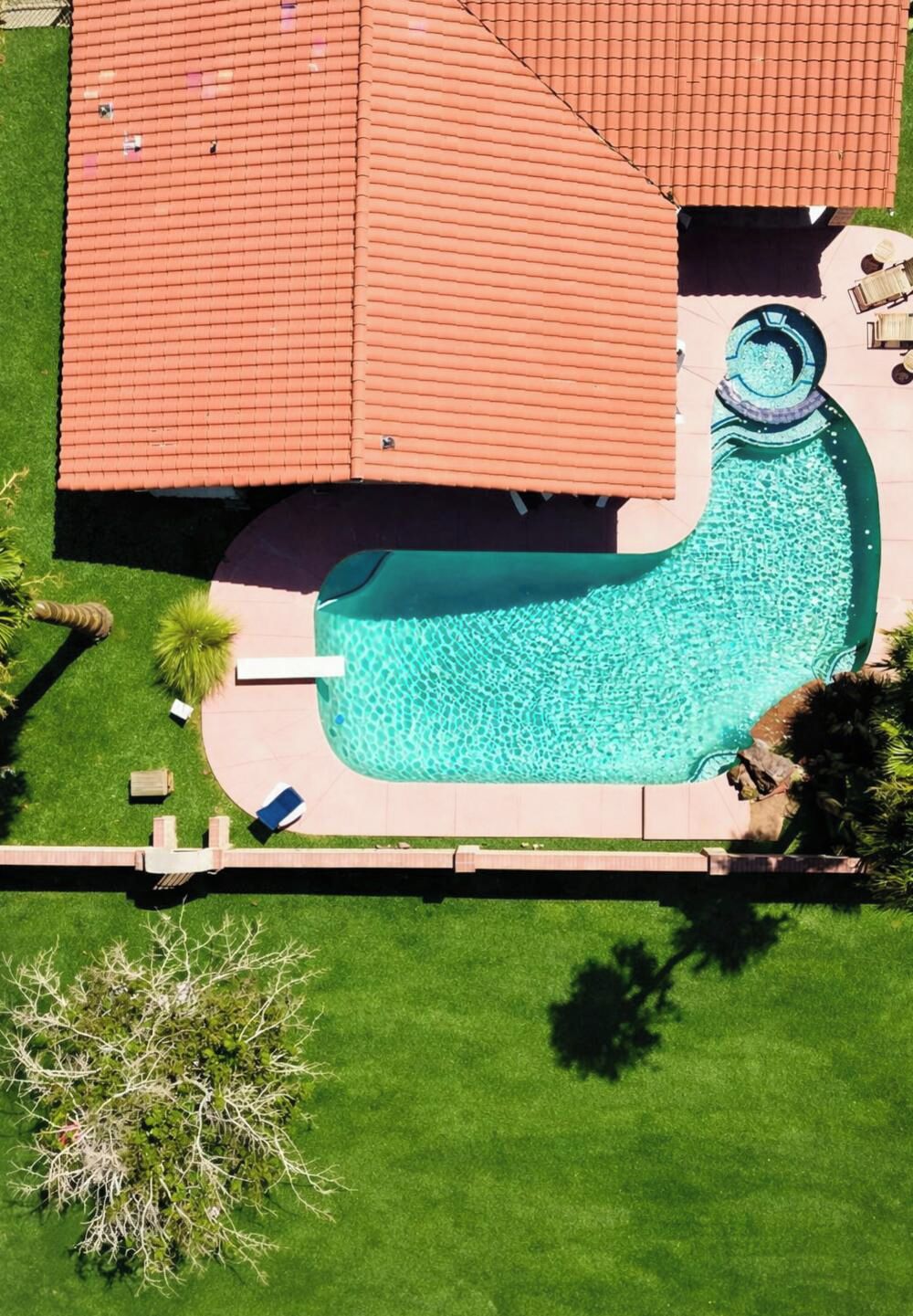 Vue aérienne d’une propriété résidentielle dotée d’une piscine, d’un toit recouvert de tuiles rouges et d’une pelouse bien entretenue.