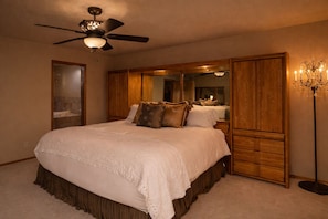 A bedroom with a large bed, a ceiling fan, a mirror, wooden paneling, and a floor lamp. - Luxury 5-Star Couples Retreat with Home Theater, Golf Course and Views. (Lake Havasu City)