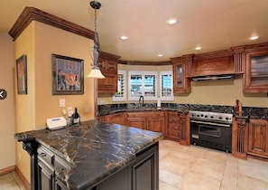 A kitchen with dark marble countertops, wooden cabinets, a built-in oven, and a pendant light. - Luxury Golf-Course Retreat — Pool, Spa, Mountain Views & Private Home Theater (Lake Havasu City)
